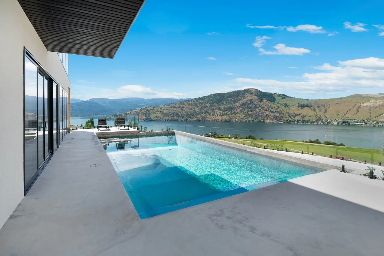 An infinity pool along the edge of a concrete deck, with Okanagan Lake and the hills beyond