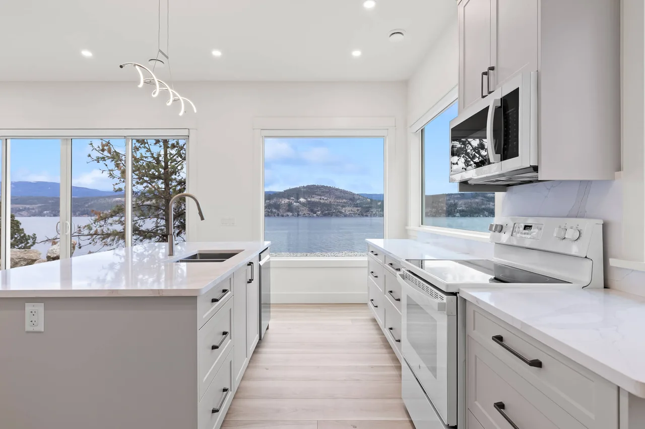 A white kitchen with a long quartz counter and windows looking straight out over the lake