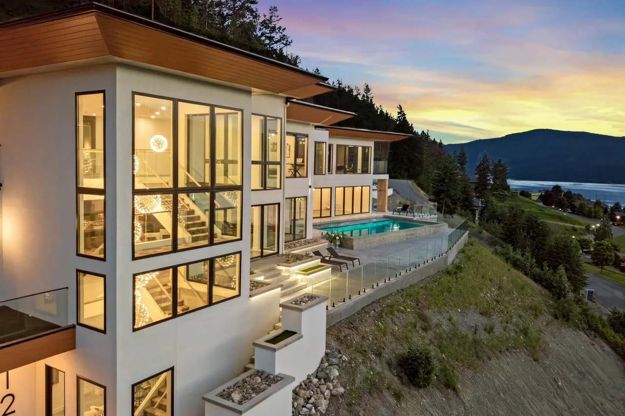 Sunset Boulevard at dusk: three storeys of lit glass above a glass-railed pool deck and the lake