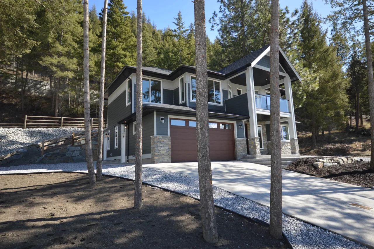 The home’s garage side, with stone and dark siding among the pines