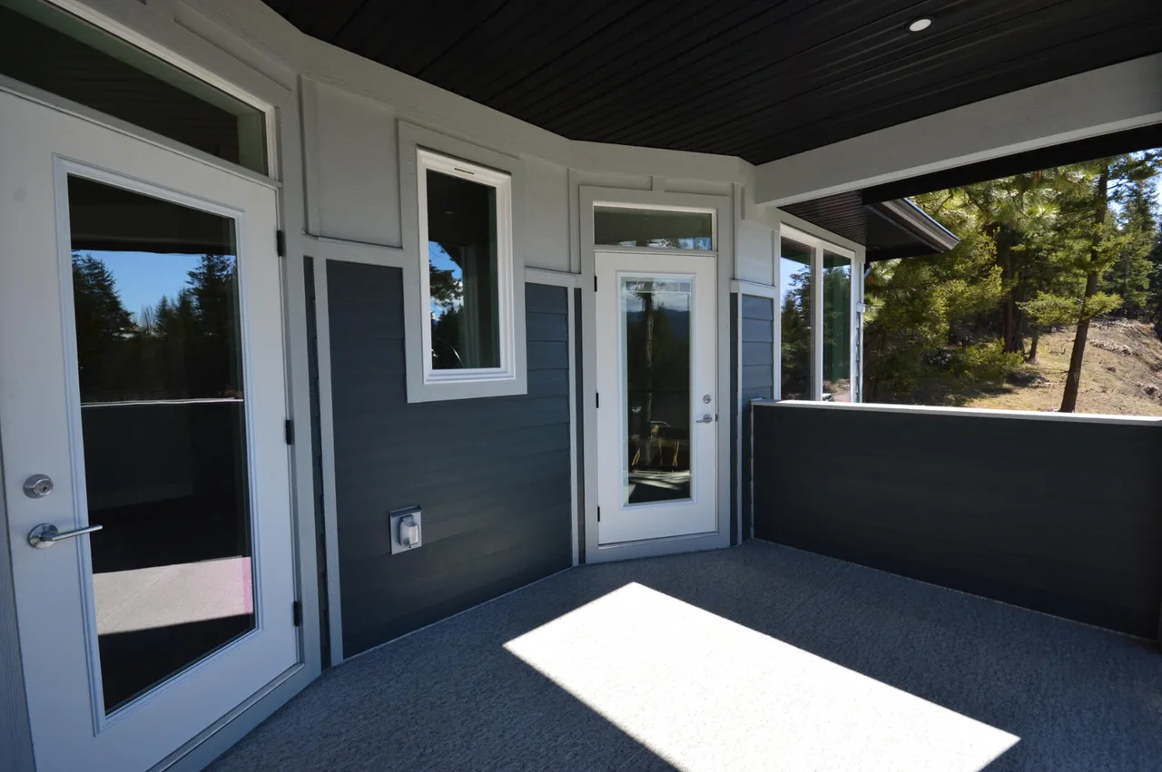 The covered deck off the main floor, with dark siding and white-trimmed doors