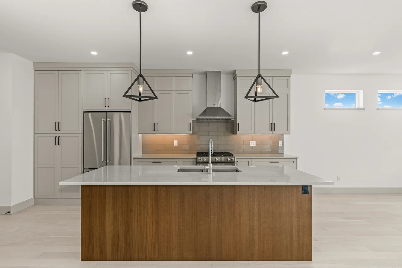 A bright kitchen with grey shaker cabinets, a walnut island with a white quartz top and two geometric pendants